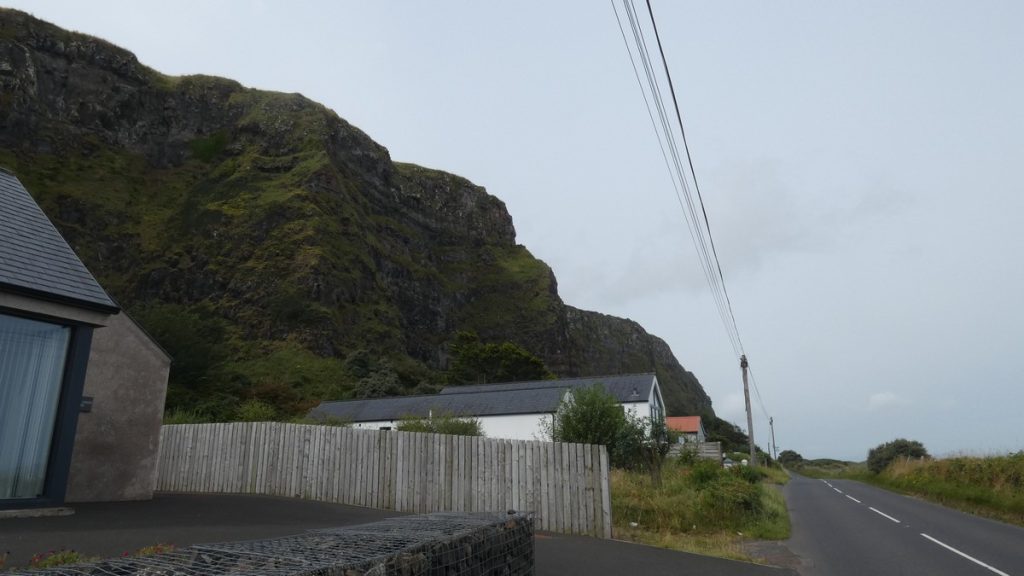 Hohe Felsen, eine Häuserzeile, Strasse, dann Strand und Meer